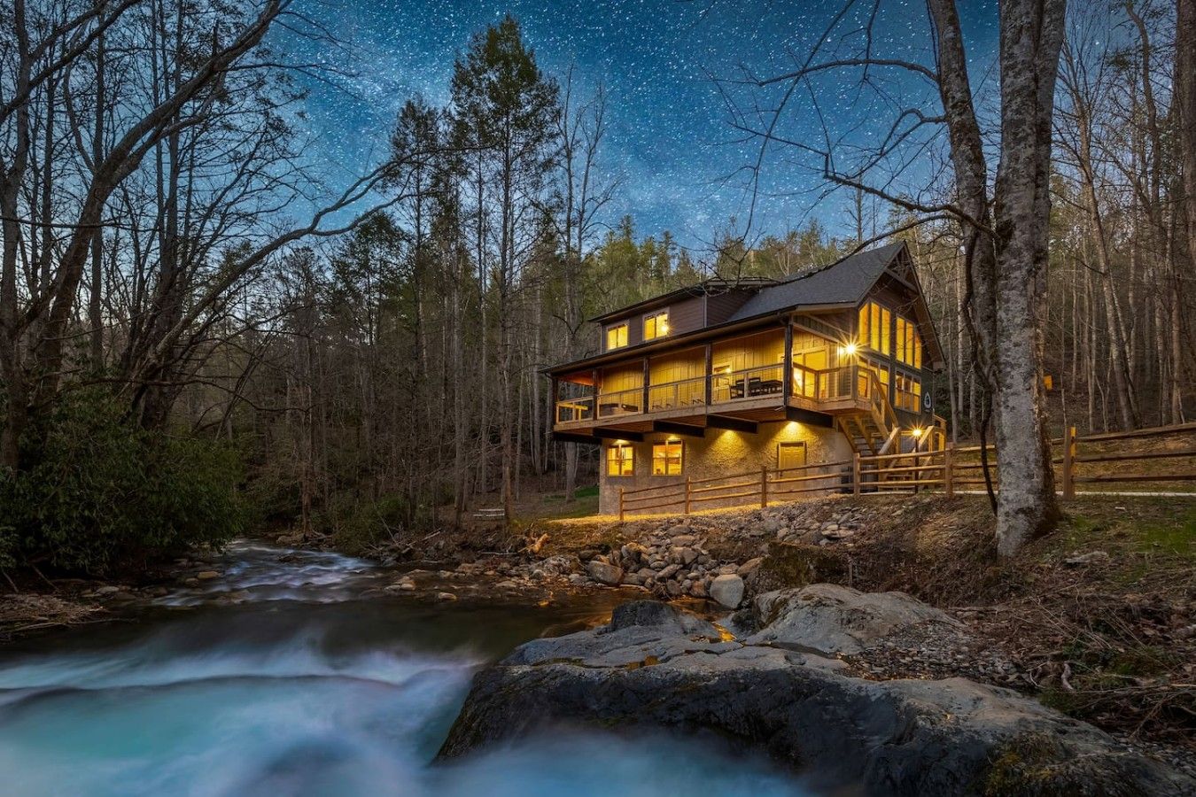 Swimming Hole Cabin lit up at dusk above the creek